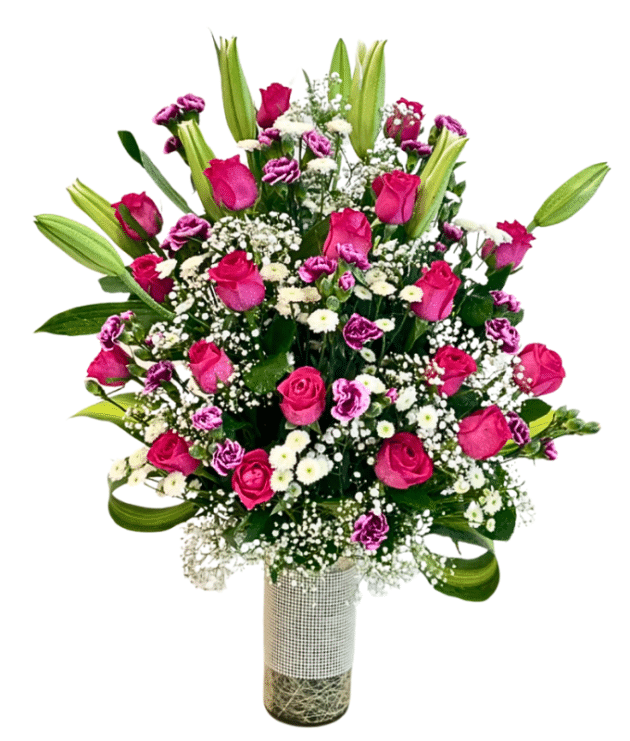 Dark pink roses,purple shaded spray carnations,white lilies arrangement in cylindrical glass vase